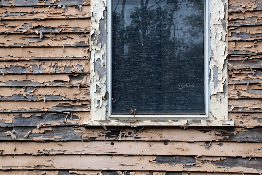 Peeling paint on weathered wooden siding near window