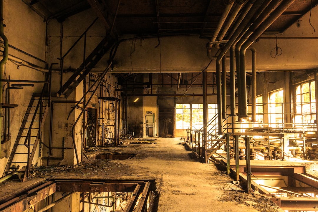 An abandoned, decaying industrial factory interior with pipes and windows.